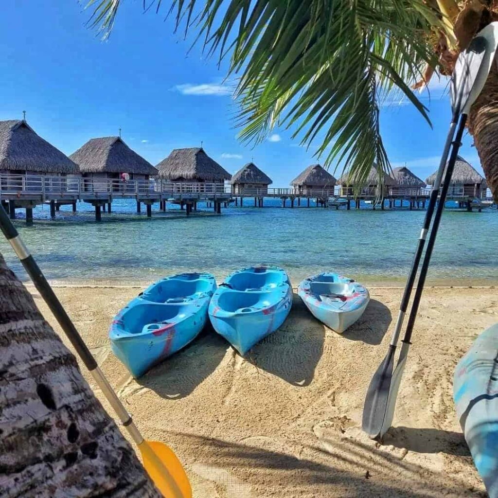 kayaks on sand and paddles beside them with Moorea Manava overwater bungalows in the background