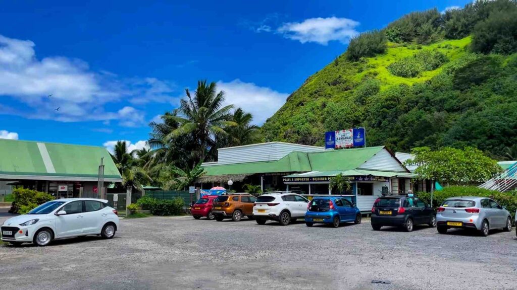Lots of Moorea rental cars at La petit village shopping center with blue skies and green mountains in the back