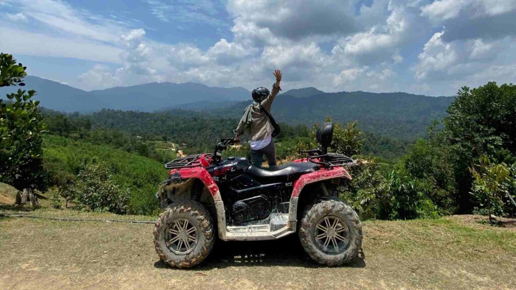 A man standing behind an ATV in Moorea with views of green mountains and cloudy sky